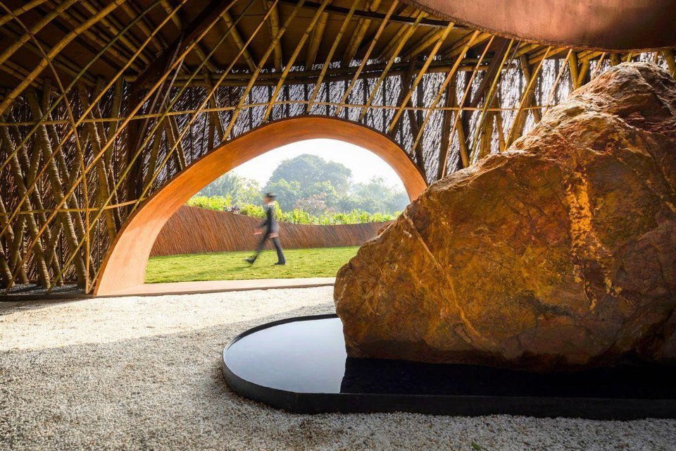 A bamboo pavilion with an arched opening onto a lawn and a large boulder
