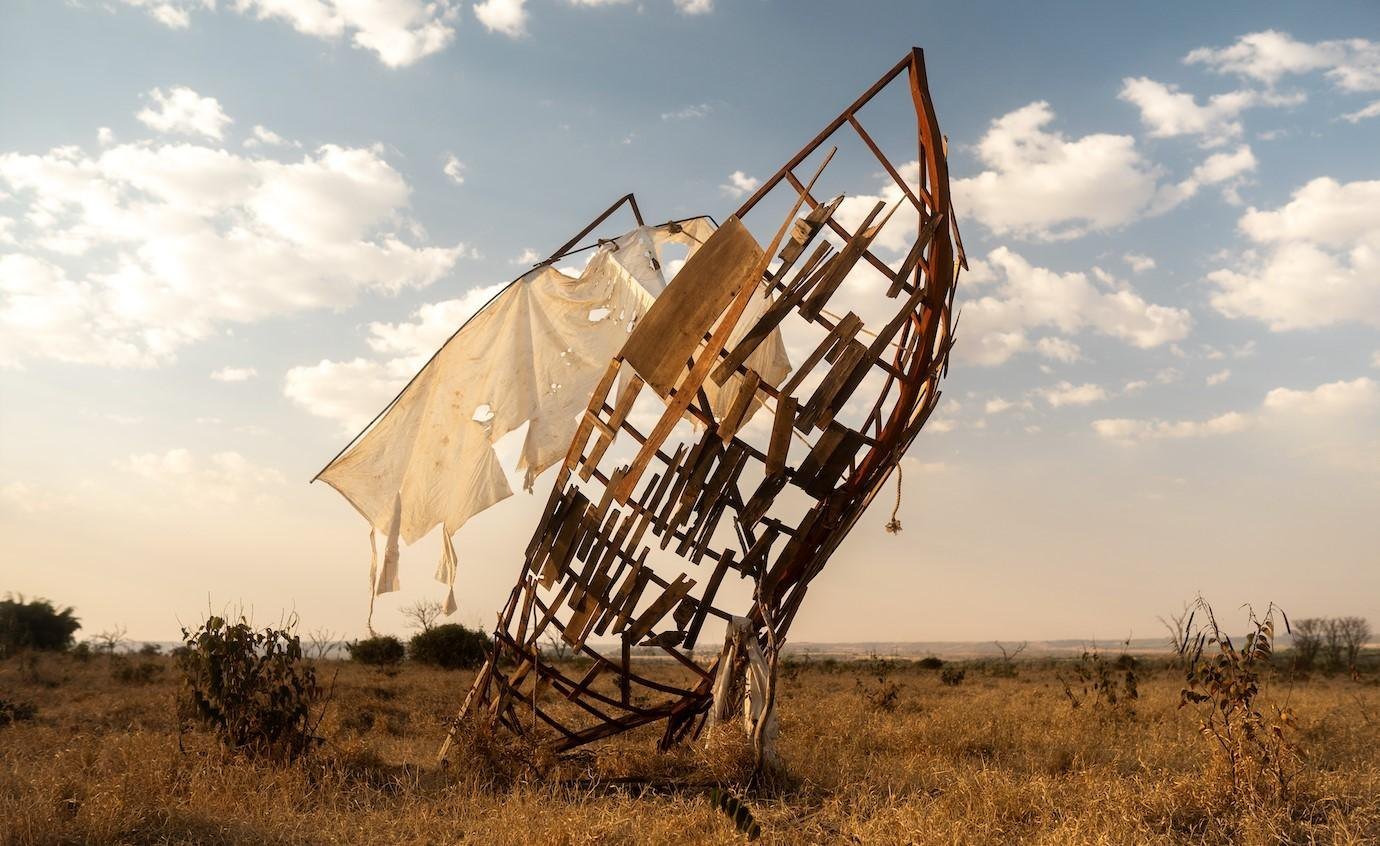 A weathered timber sculpture rising over a dry grassland at dusk