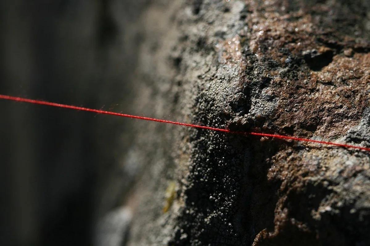 A single red thread stretched across a weathered rock surface